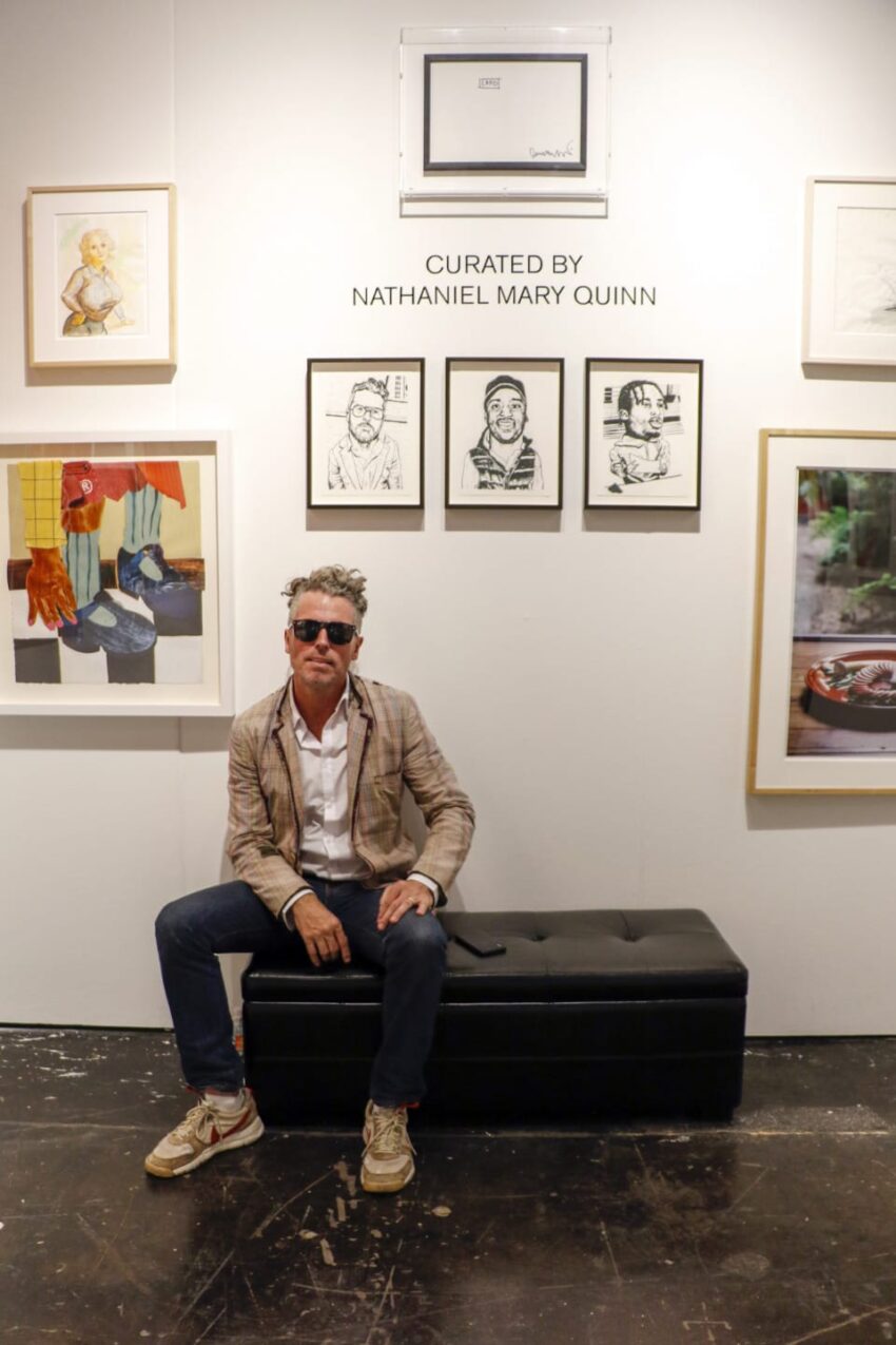 Person sitting on a black bench in an art gallery with various framed artworks on the wall behind them.