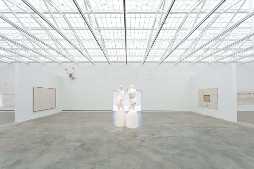 Modern art gallery with white walls featuring two abstract statues in the center under a bright, grid-patterned ceiling.
