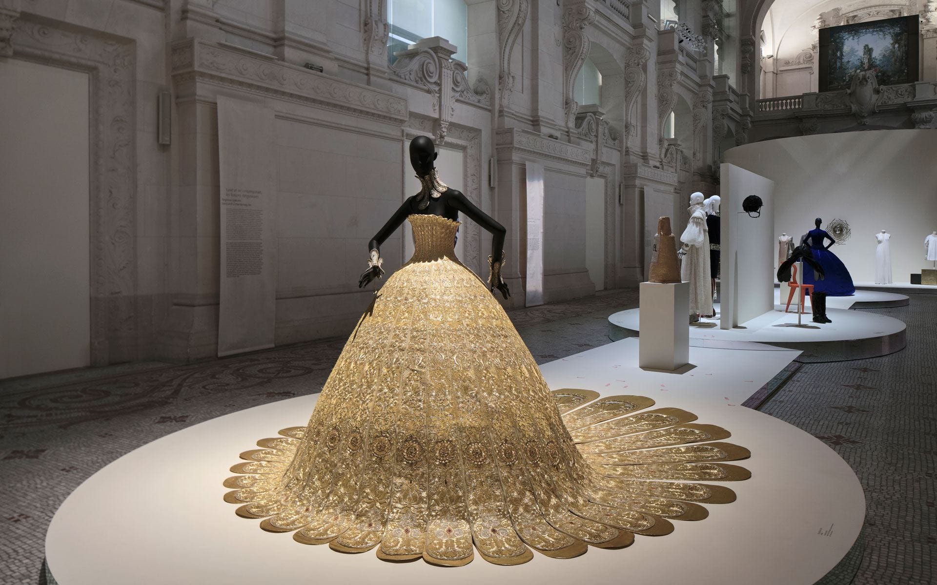 Exhibit of ornate golden gown in an elegant museum gallery setting.