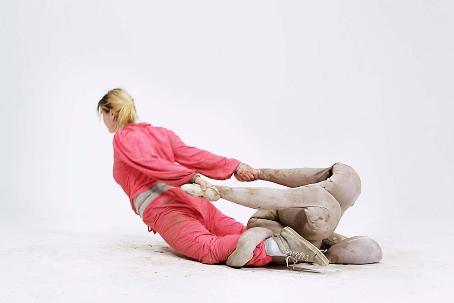Person in pink suit poses creatively with artistic sculpture against a white background.