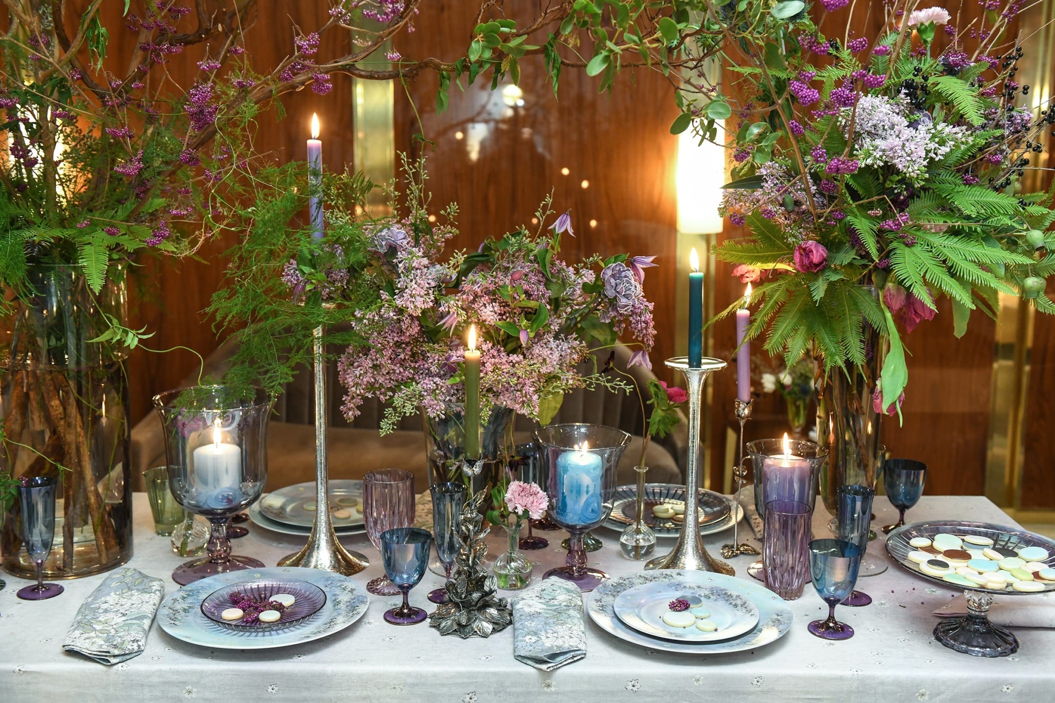 Elegant dinner table with floral centerpieces, candles, glassware, and decorative plates set for an upscale event.