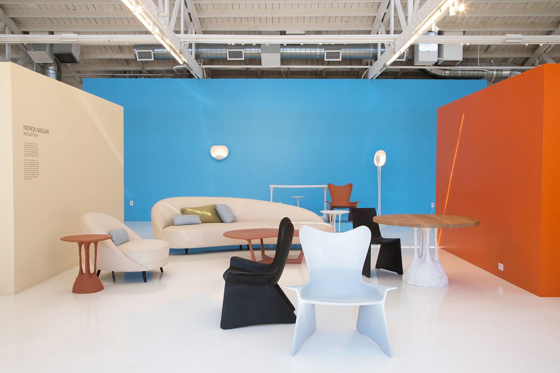 Modern furniture showroom with colorful walls, featuring various chairs, tables, and a sofa on a glossy white floor.