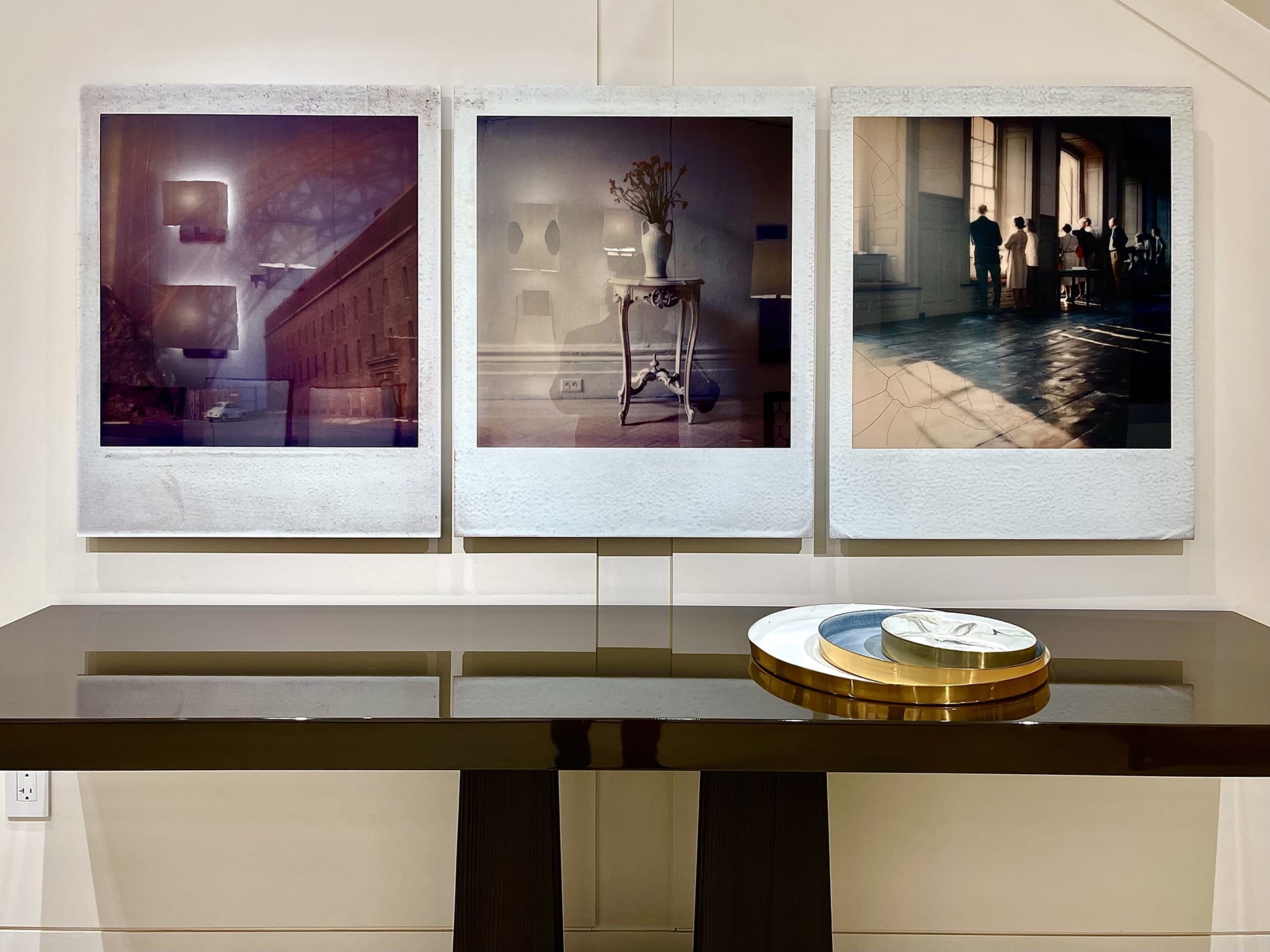 Three framed photos above a sleek wooden table with decorative trays in a modern interior.