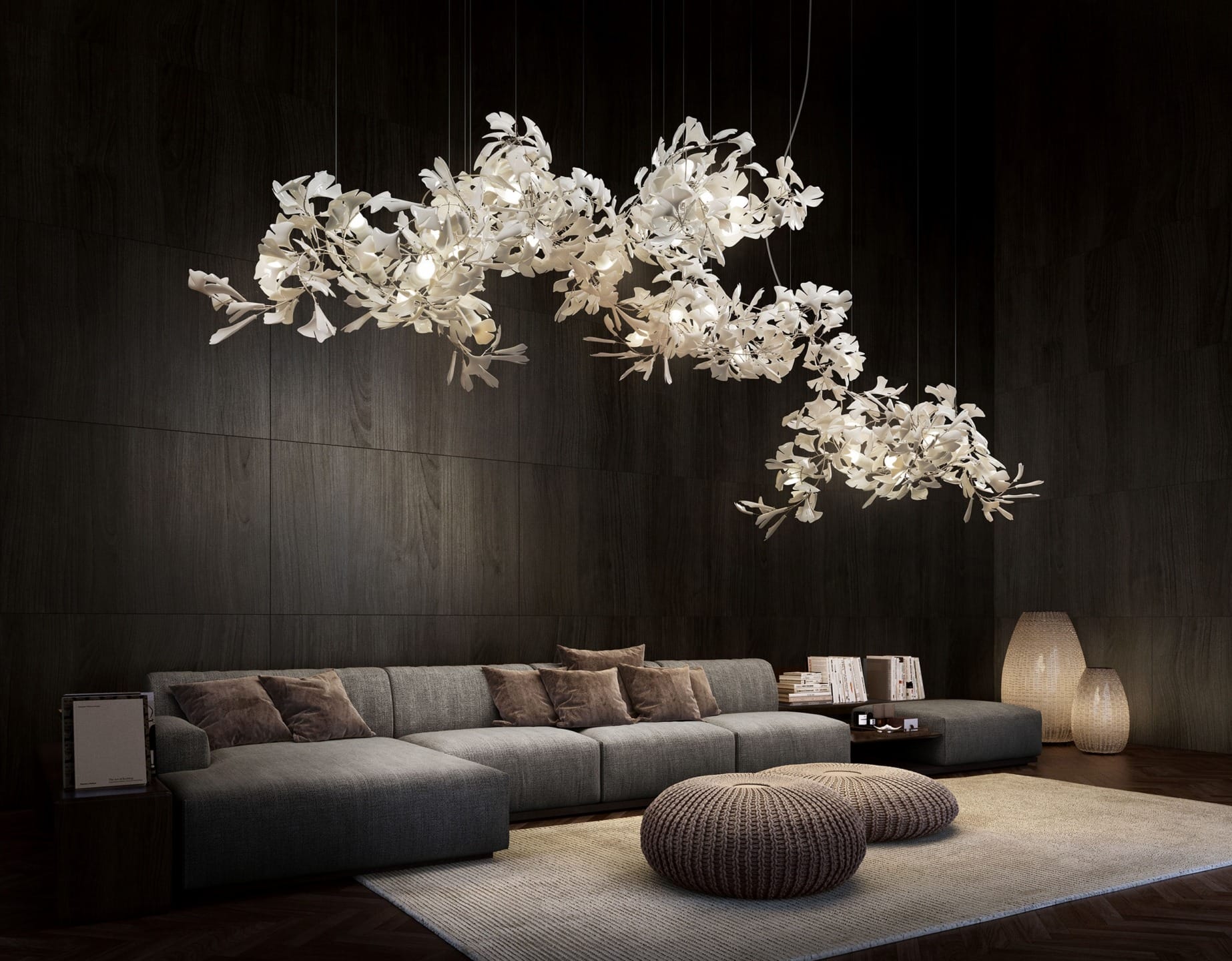 Modern living room with dark wood walls, gray sectional sofa, white floral chandeliers, wicker poufs, and soft lighting.