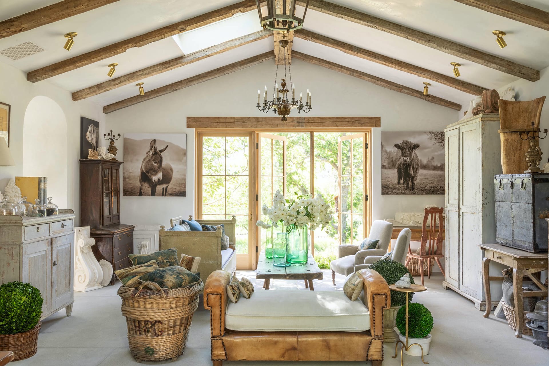 Rustic living room with large windows, wooden beams, cozy furniture, and animal artwork on the walls.
