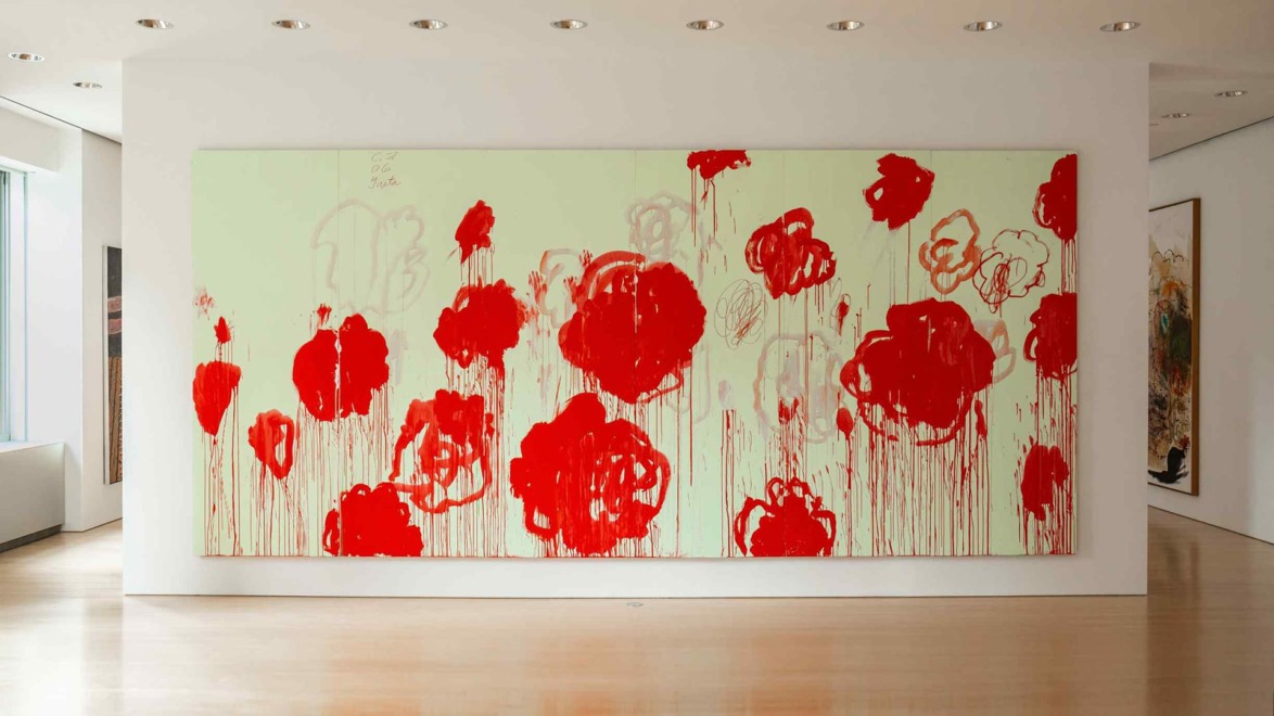 Large abstract painting with bold red flowers on a light green background, displayed in a well-lit modern gallery.