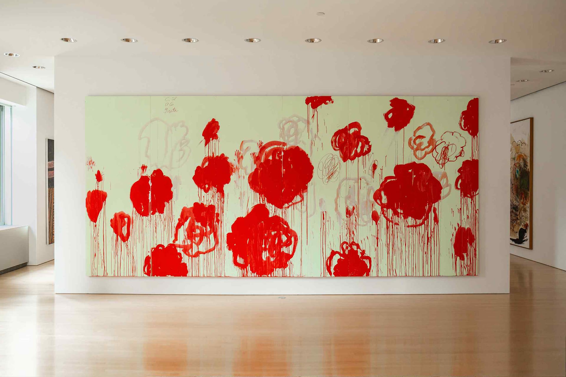 Large abstract painting with bold red flowers on a light green background, displayed in a well-lit modern gallery.