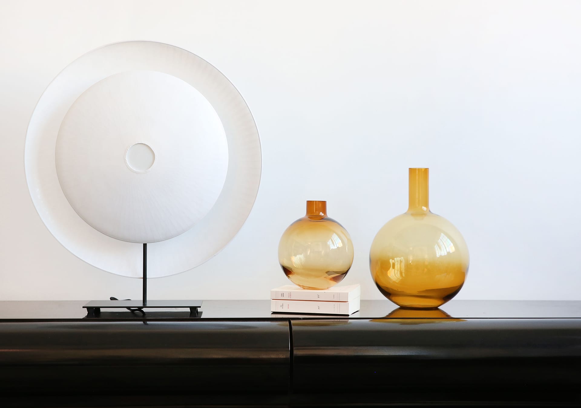Modern decor with a large white disc on a stand and two amber glass vases on a sleek black shelf.