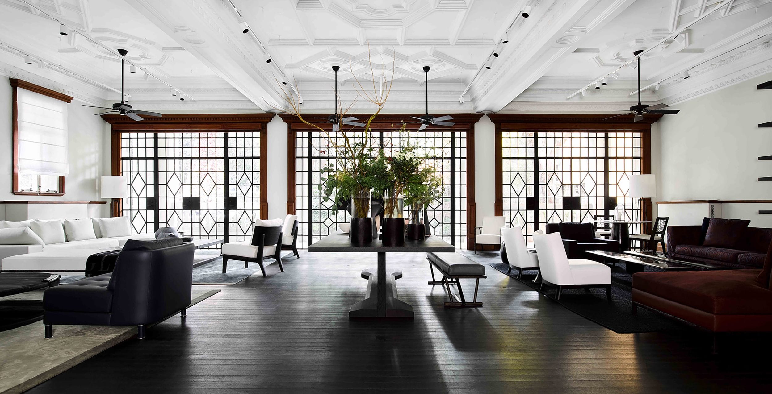 Luxury living room with modern furniture, large windows, elegant ceiling, and central table with decorative plants.