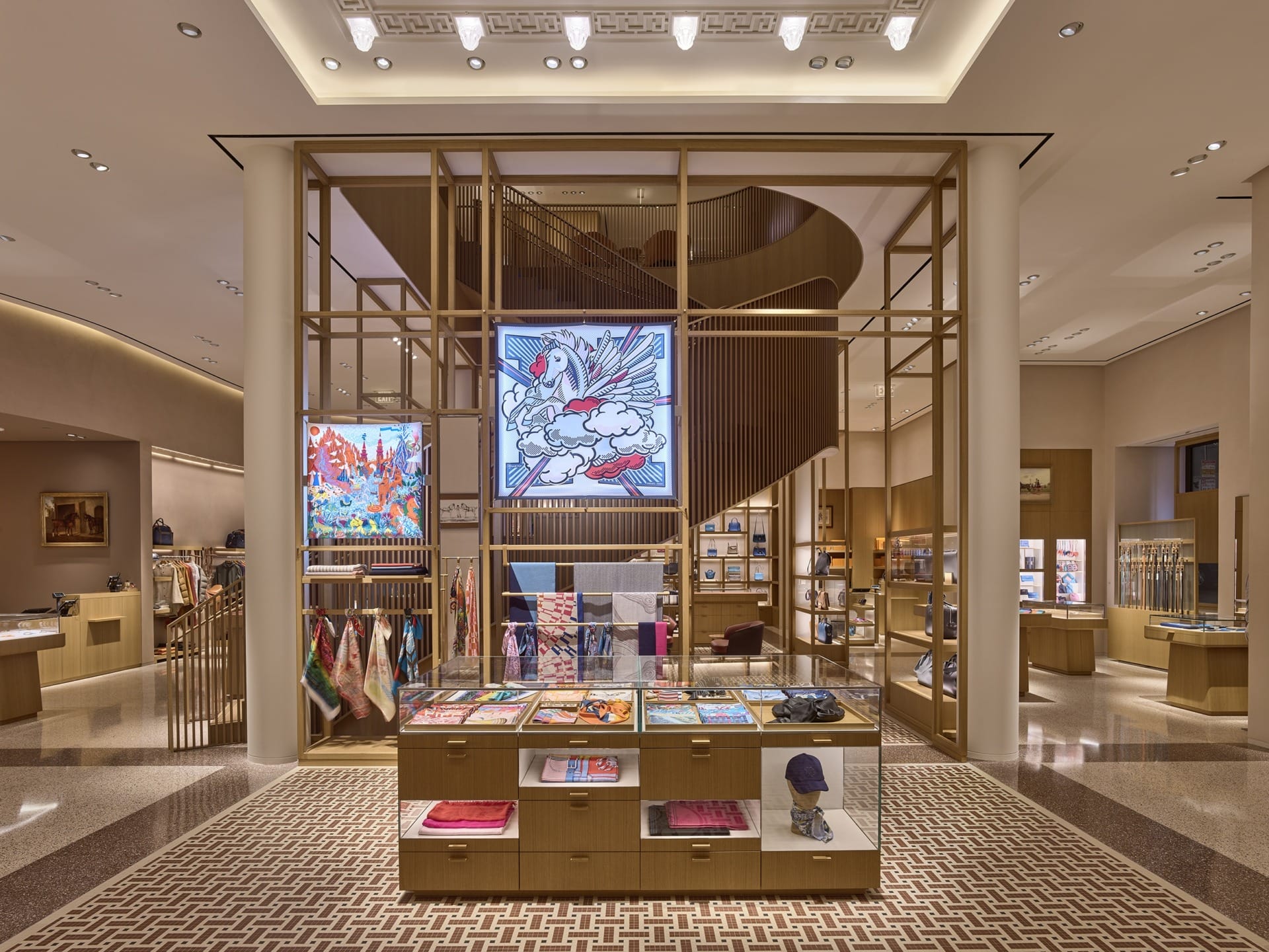 Luxury retail store interior with displays of colorful scarves, accessories, and artwork, featuring elegant lighting and decor.