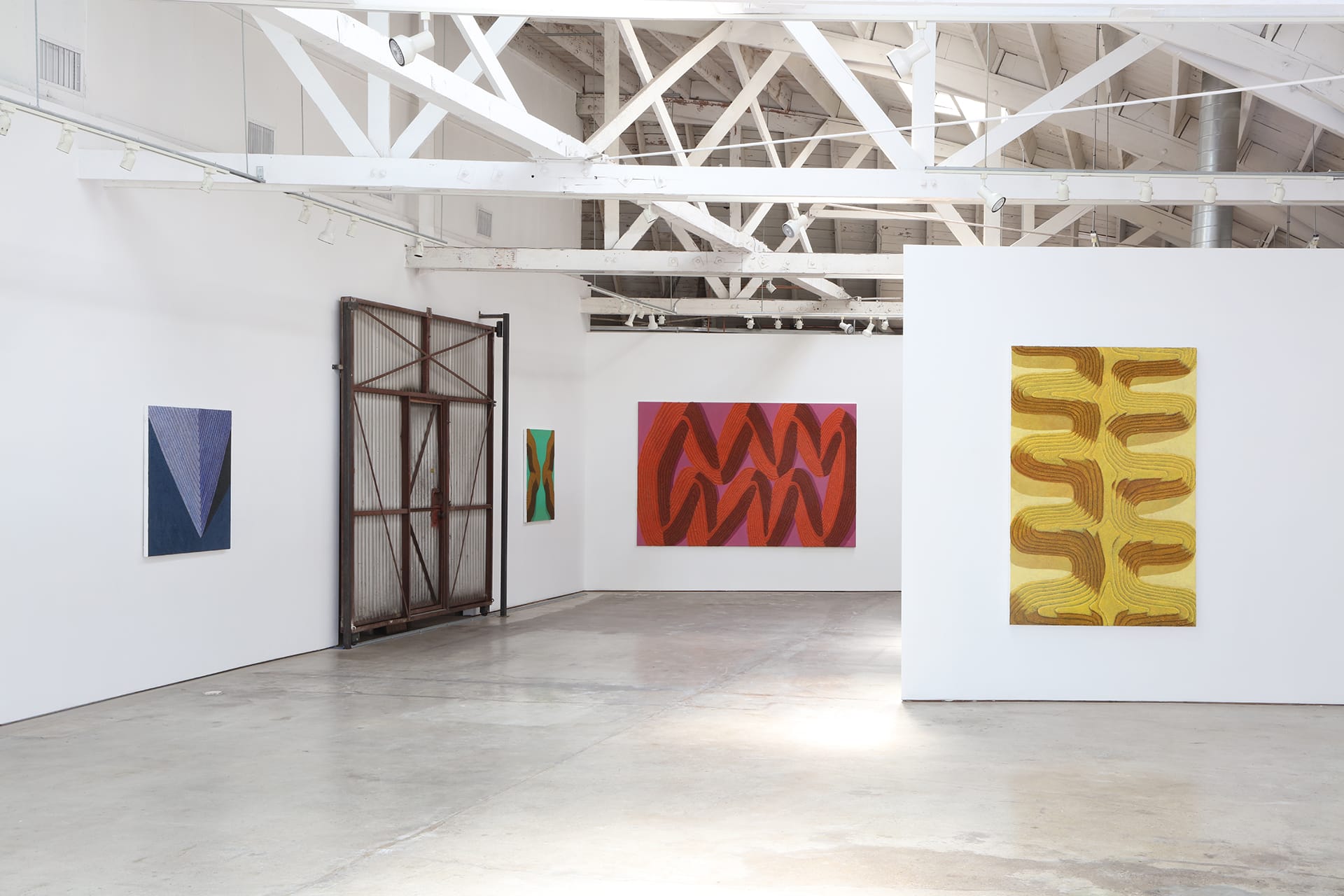 Spacious art gallery with contemporary abstract paintings on white walls and exposed ceiling beams.