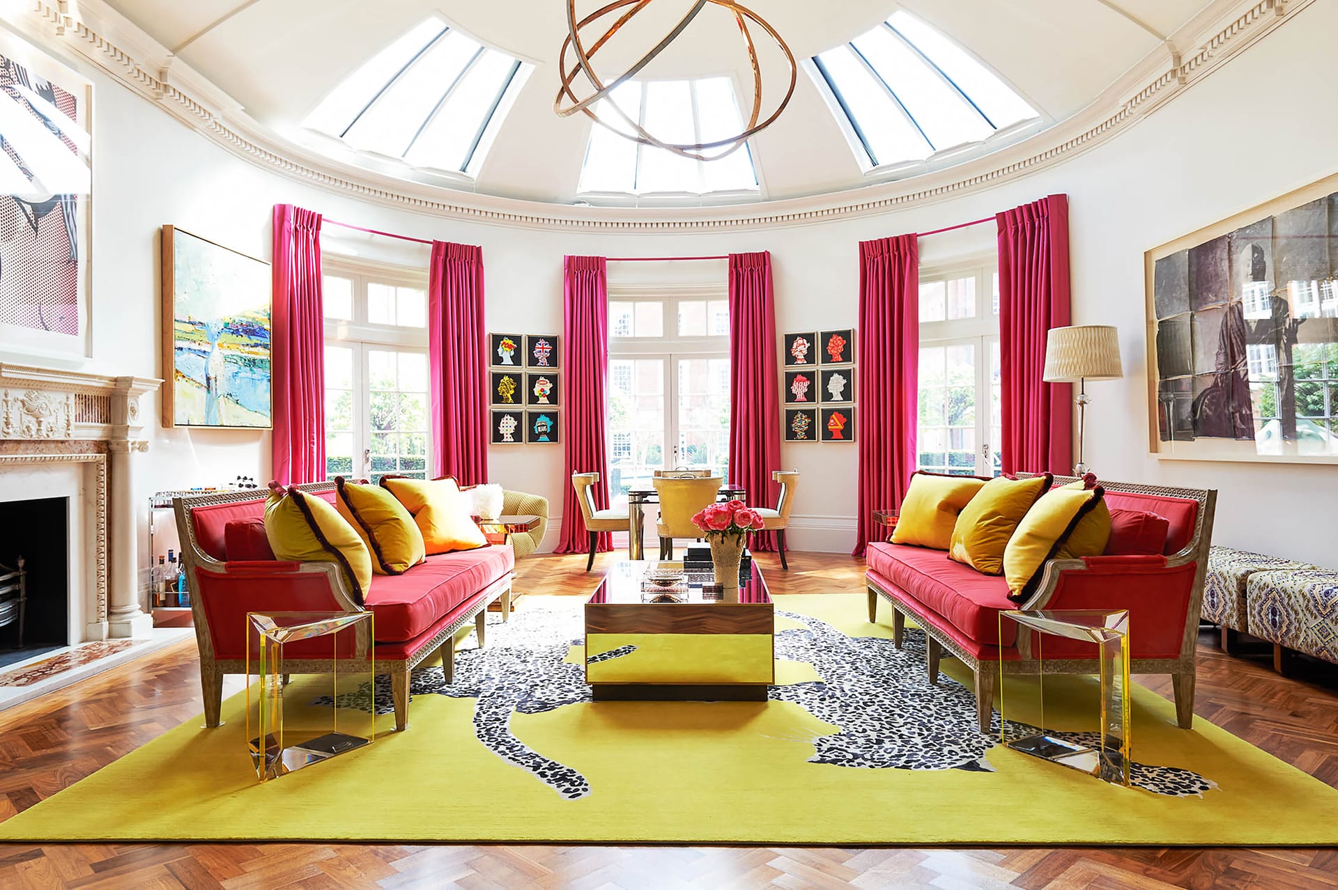 Colorful living room with red sofas, yellow pillows, large windows, pink curtains, modern art, and a bright yellow rug.