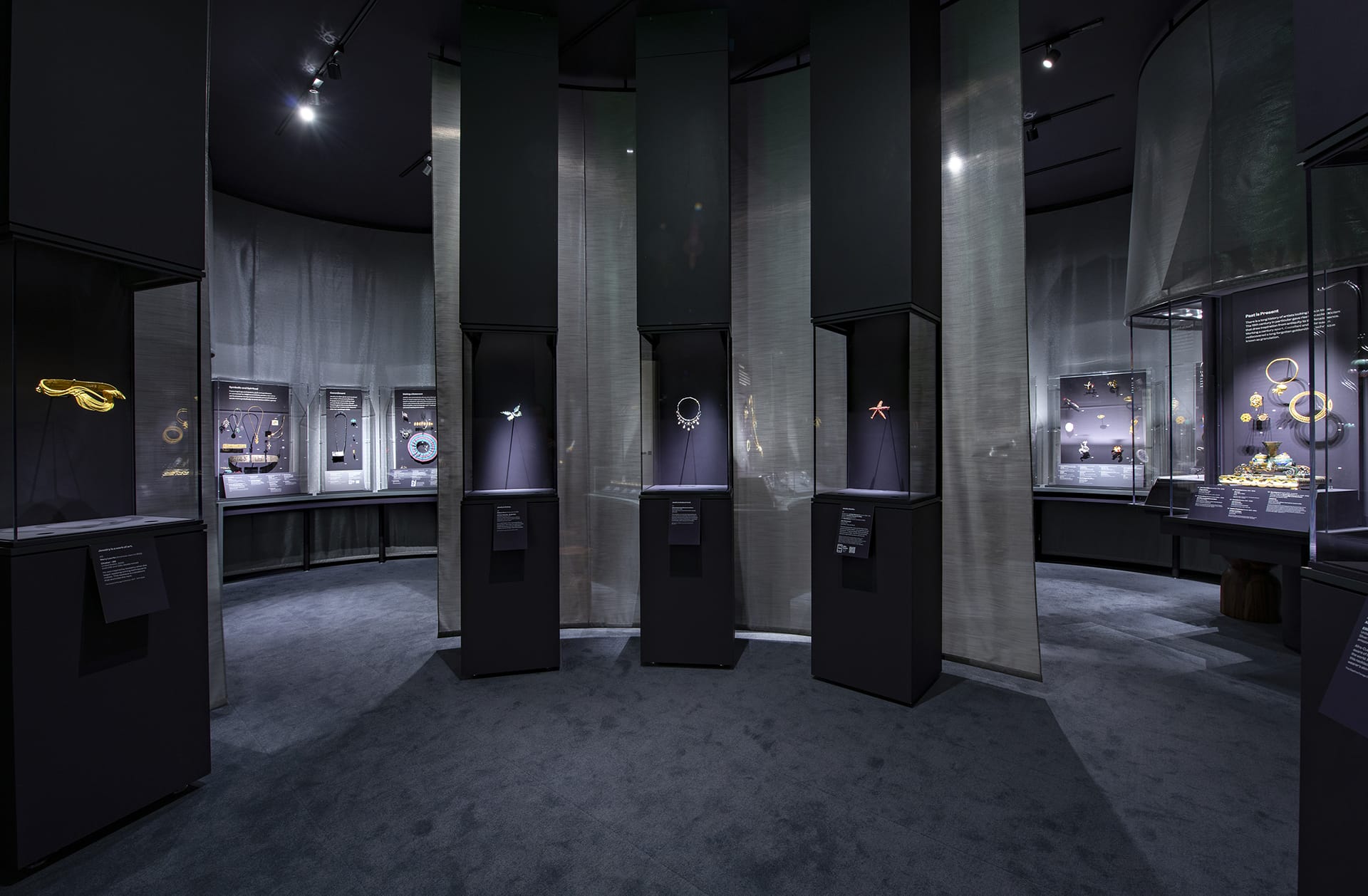 Museum exhibit showcasing modern jewelry displayed in sleek cases with dim lighting and a sophisticated atmosphere.