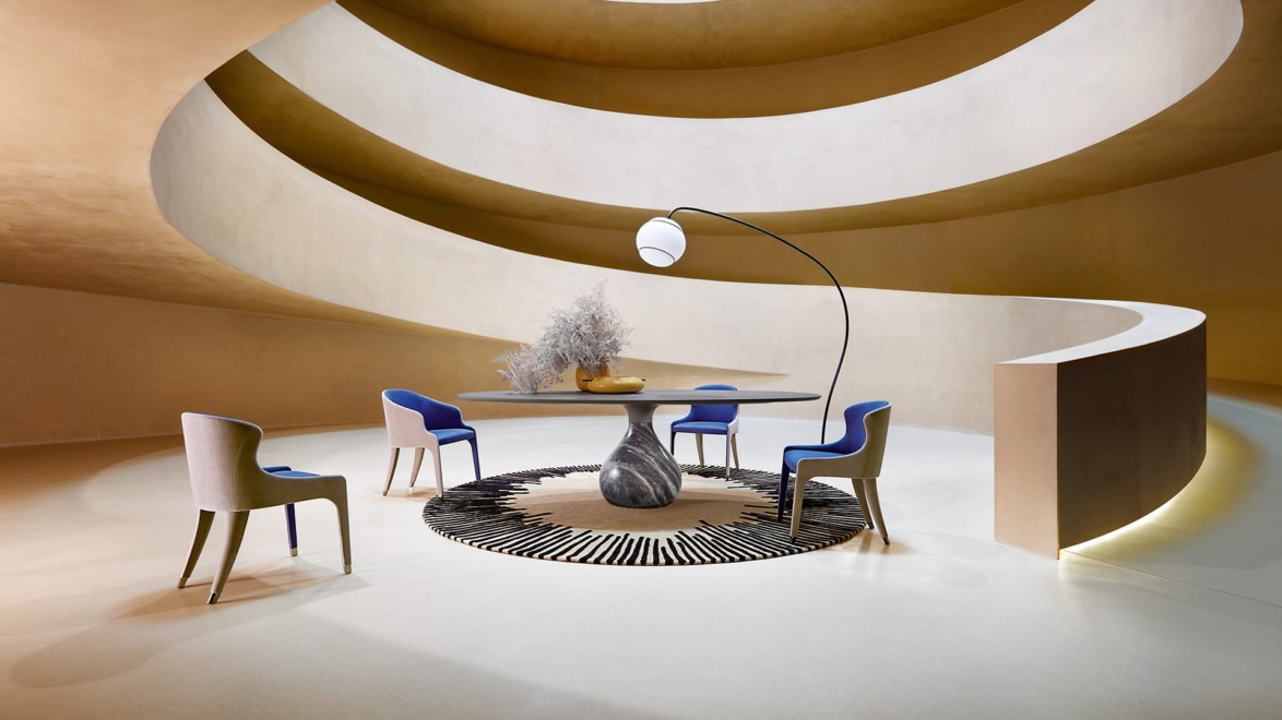 Modern spiral interior with a round table, blue and beige chairs on a patterned rug, and a unique floor lamp.