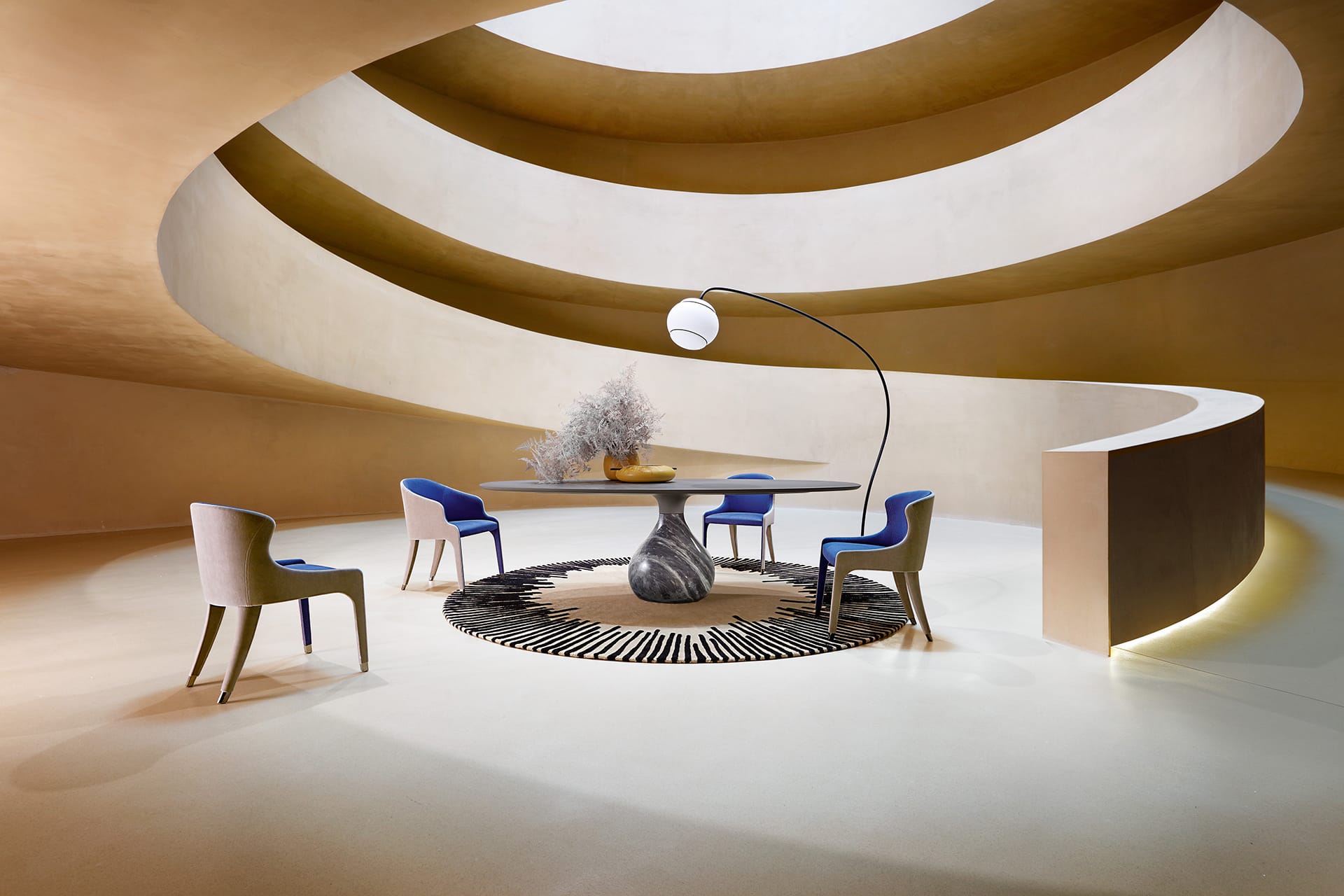 Modern spiral interior with a round table, blue and beige chairs on a patterned rug, and a unique floor lamp.