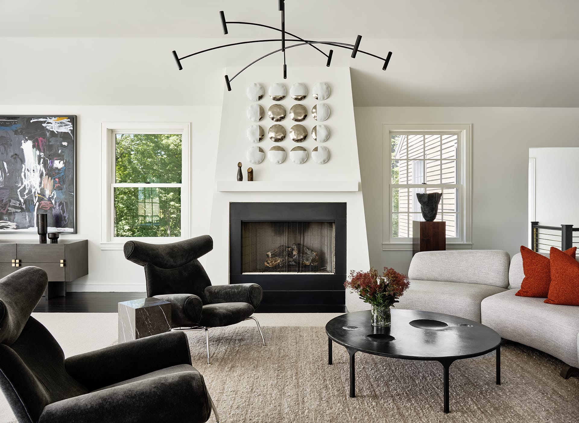 Modern living room with abstract chandelier, black and white furniture, and art above fireplace mantel.