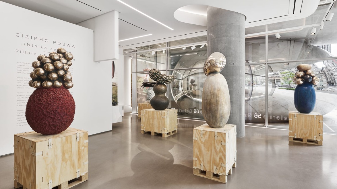 Art gallery exhibit with four abstract sculptures on wooden pedestals, featuring various textures and metallic elements.
