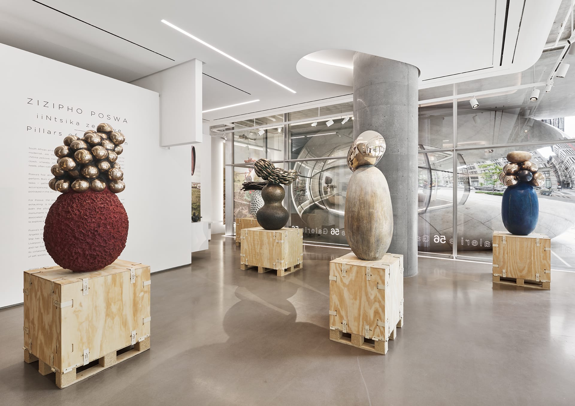 Art gallery exhibit with four abstract sculptures on wooden pedestals, featuring various textures and metallic elements.
