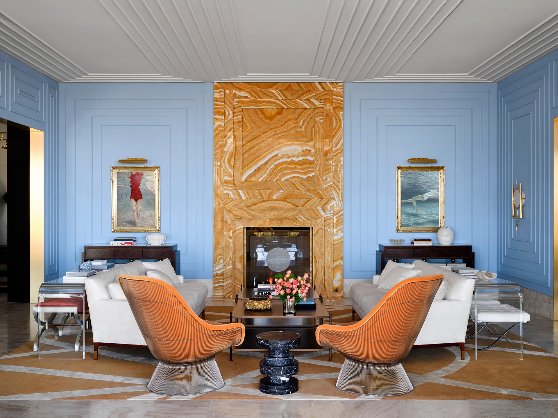 Elegant living room with blue walls, orange stone fireplace, modern chairs, beige sofas, and art pieces near bookshelves.