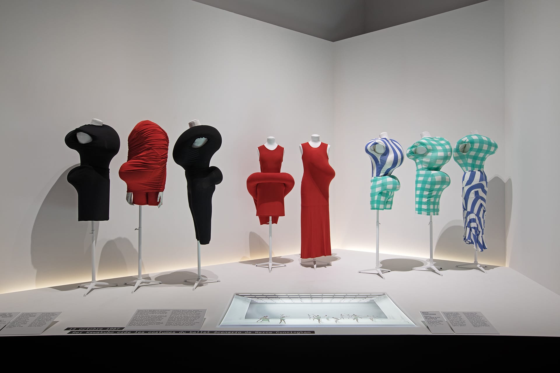 Exhibit of abstract fashion mannequins in red, black, and green checkered outfits displaying creative dress designs.