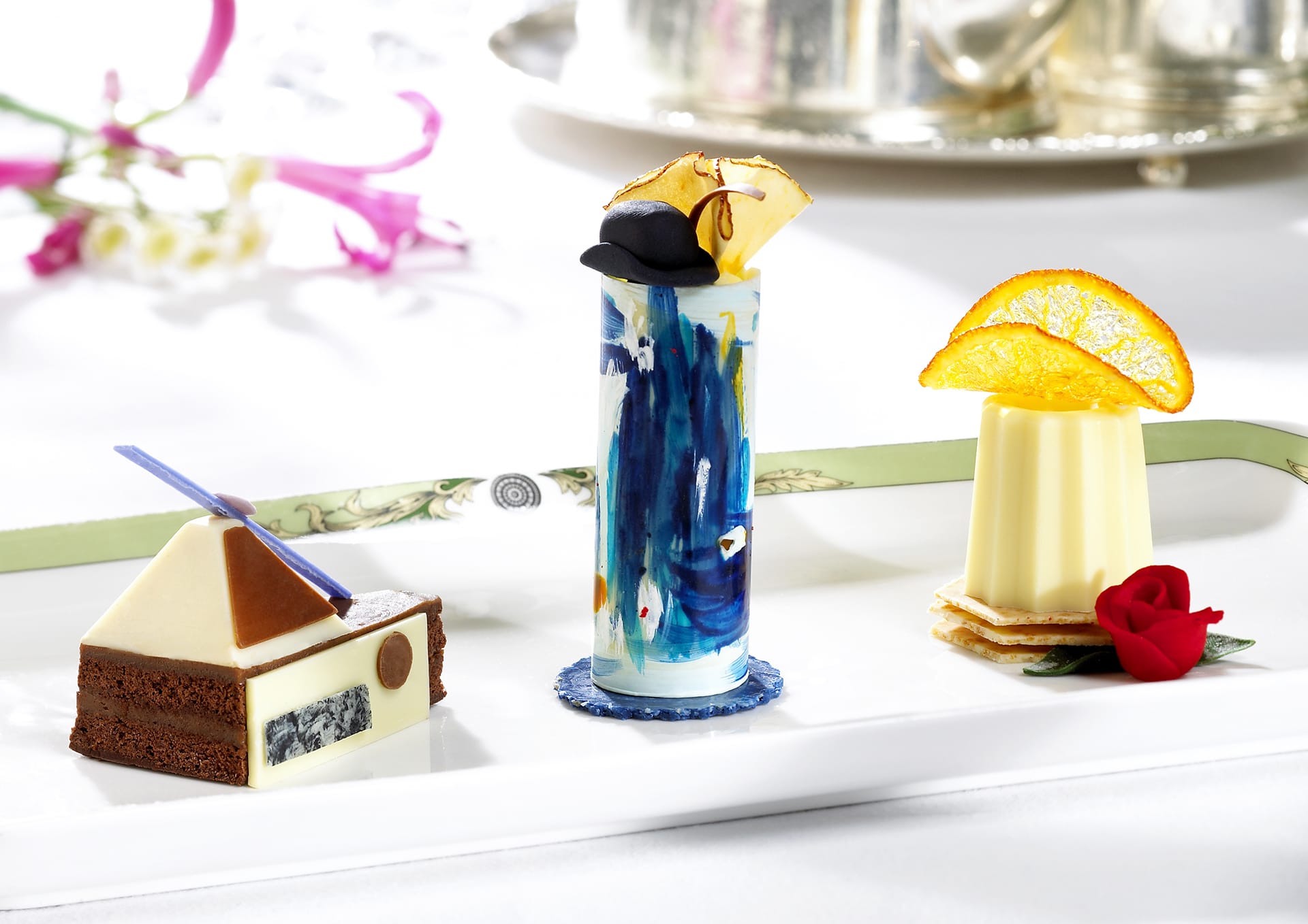 Elegant dessert trio with chocolate cake, artistic parfait, and citrus panna cotta on a decorative plate.