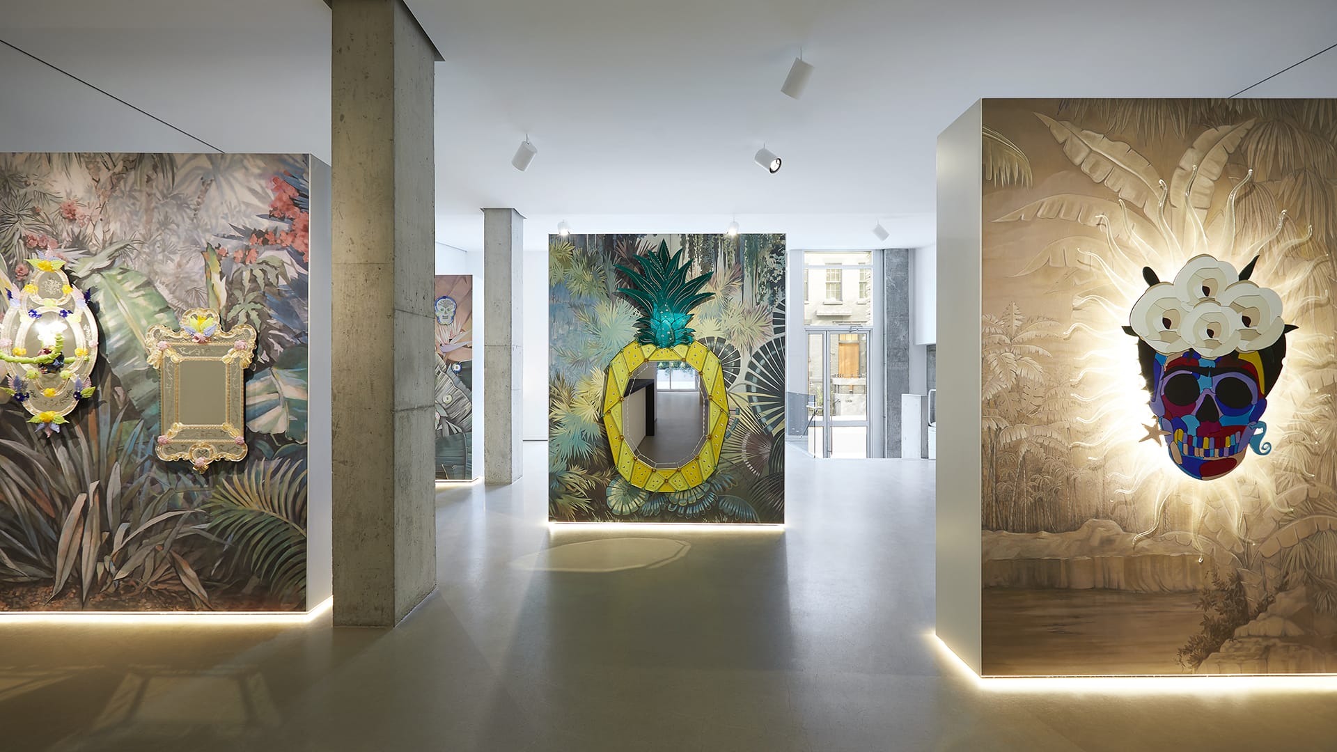 Art installation featuring vibrant, tropical-themed wall art and sculptures with pineapple and skull motifs in a modern gallery setting.