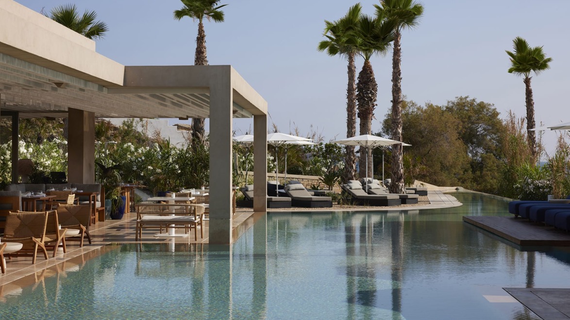 Luxurious outdoor pool area with lounge chairs, umbrellas, and palm trees under a clear sky.