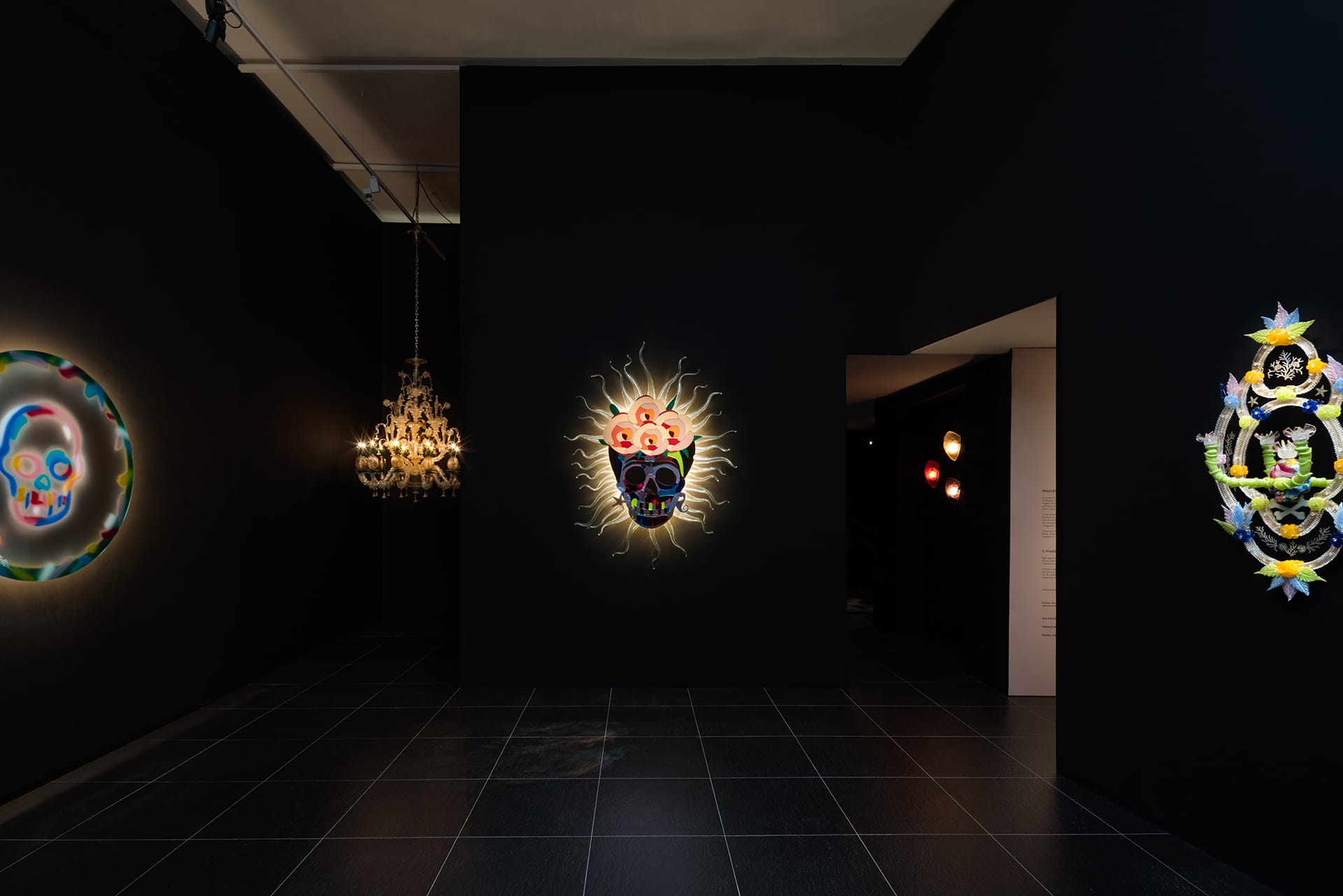 Dimly lit art gallery with colorful illuminated skull artwork on dark walls.