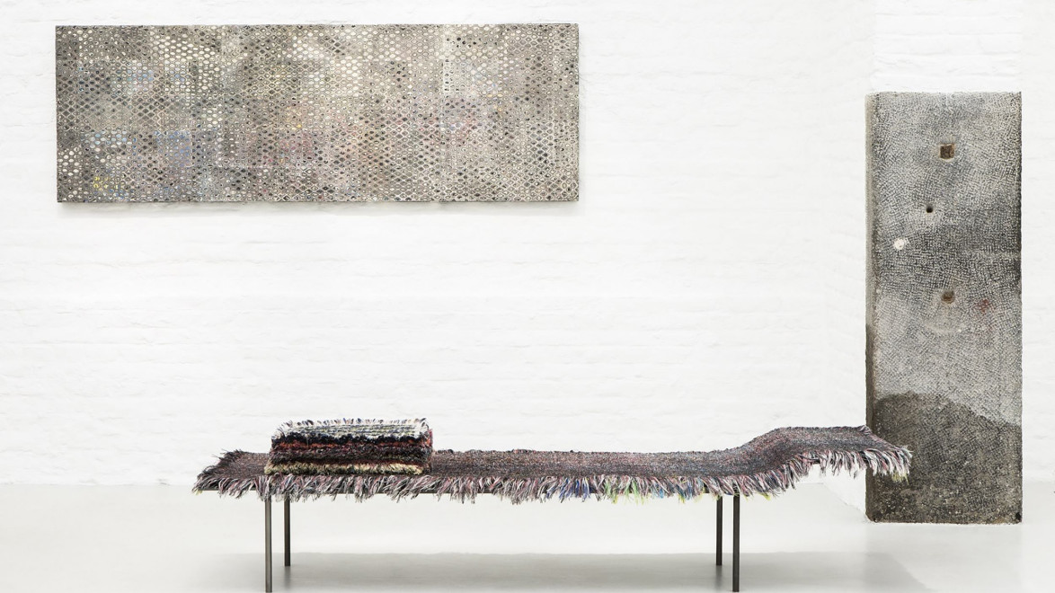 Art installation with a modern abstract painting on wall, textured sculpture, and a fringed bench with folded textile.
