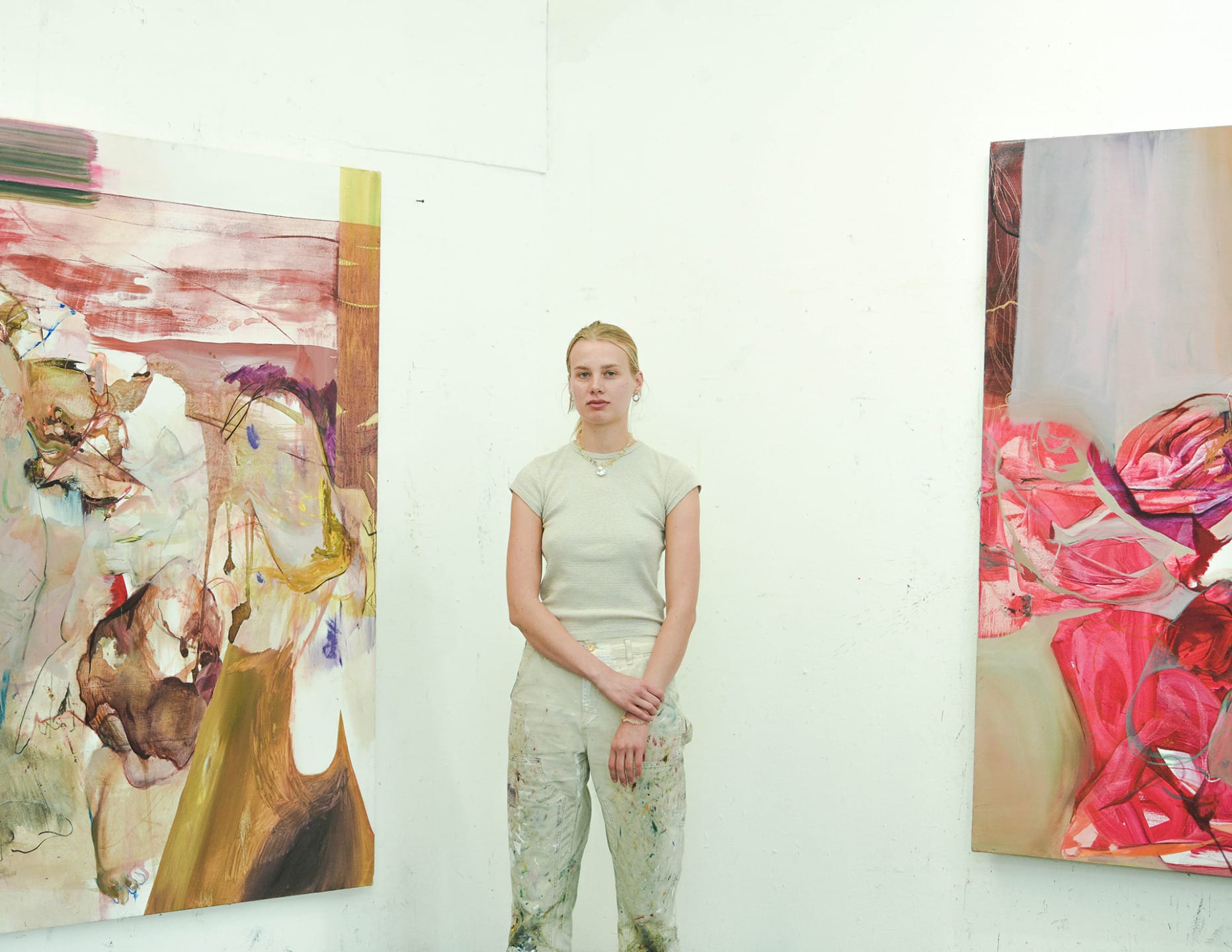 Artist standing in studio between two abstract paintings on a white wall.