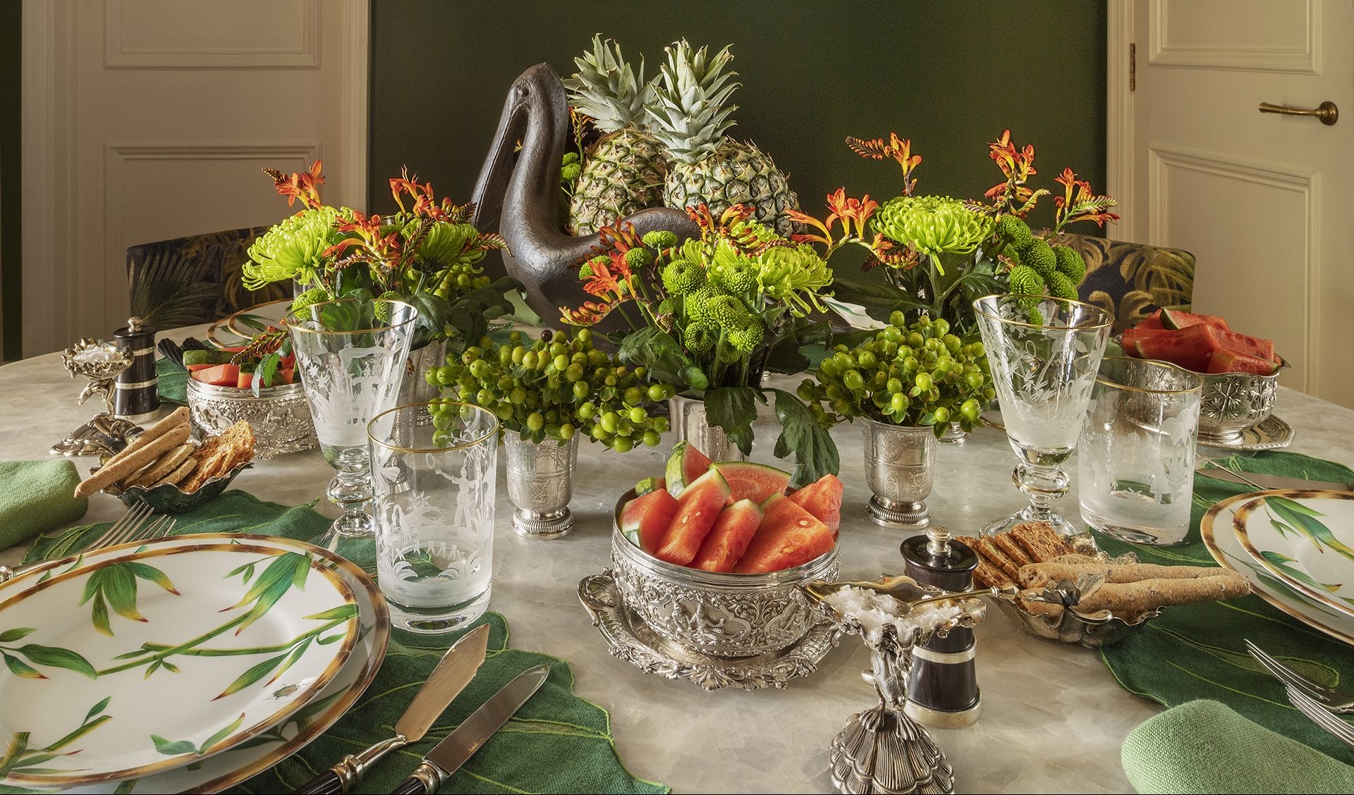 Elegant dining table set with plates, glasses, and a centerpiece of pineapples, flowers, and greenery.