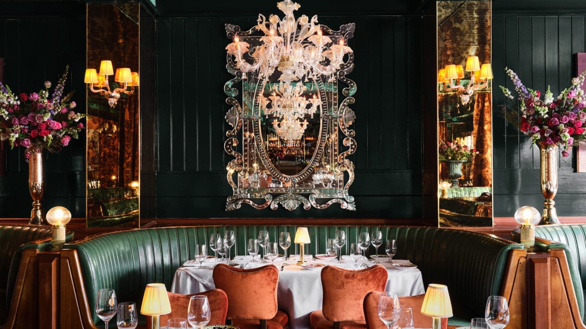 Elegant restaurant interior with chandelier, green booths, floral arrangements, mirrors, and table settings.