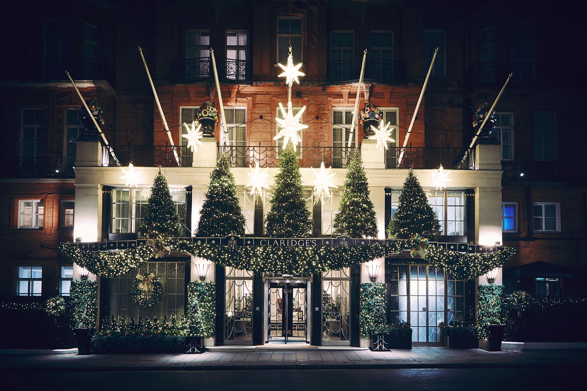 Exterior of a grand hotel adorned with elaborate Christmas decorations and twinkling star lights at night.
