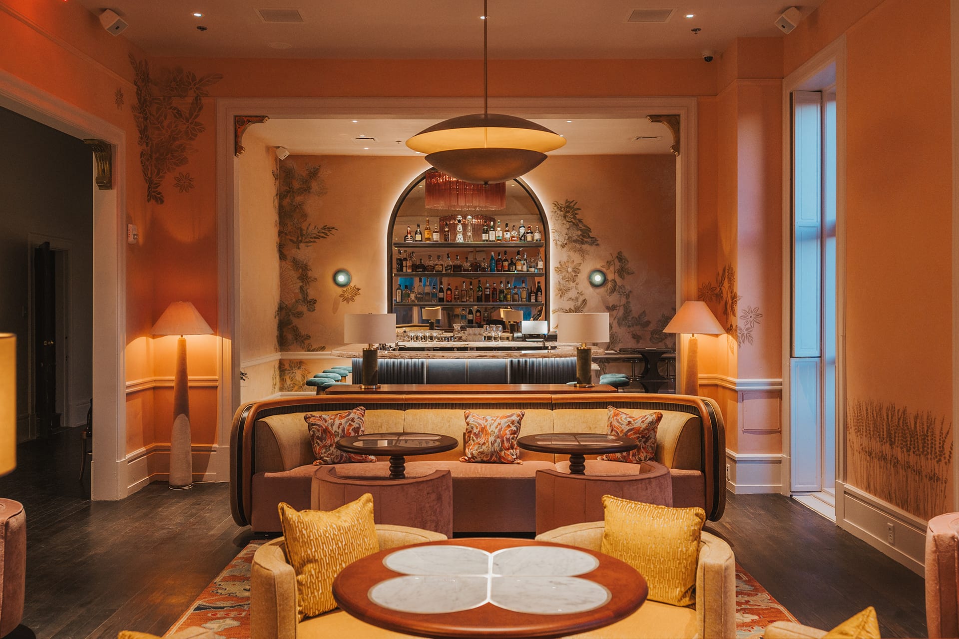 Elegant lounge area with cozy seating, decorative cushions, ambient lighting, and a well-stocked bar in the background.