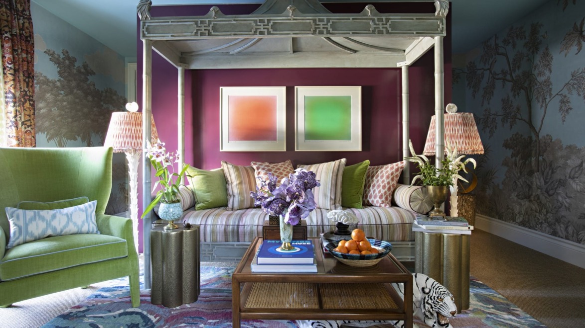 Eclectic living room with a canopy daybed, colorful cushions, vibrant rug, green armchair, and decorative lamps.