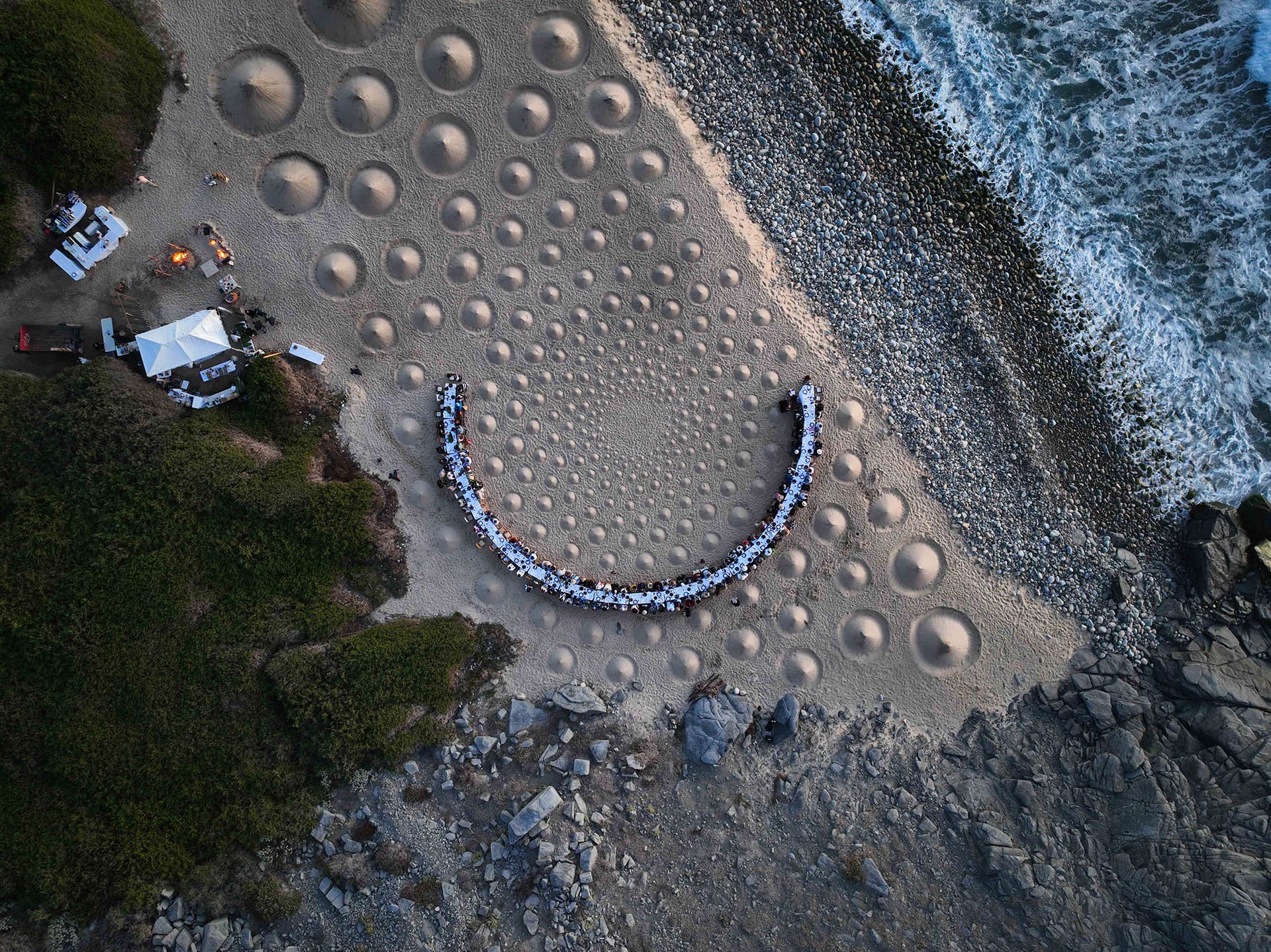 Aerial view of a beach dinner set-up with concentric sand patterns near the ocean.
