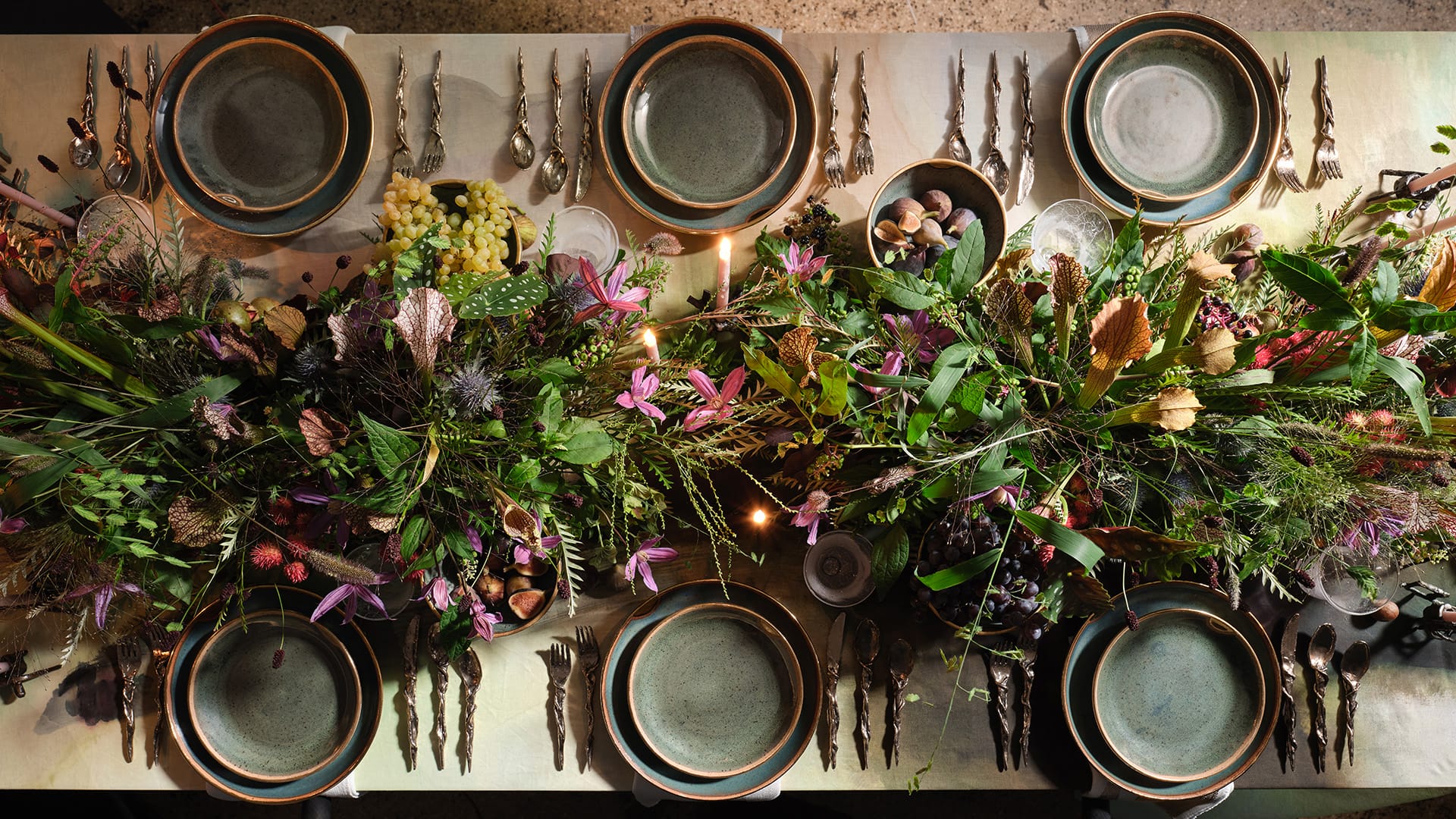 Top view of a dining table with green plates, cutlery, and a lush floral centerpiece featuring various vibrant flowers and foliage.