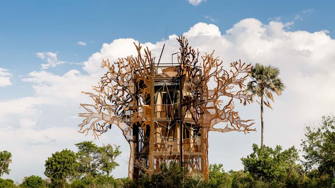 Observation tower surrounded by metal tree sculpture and lush greenery under a blue sky with clouds.