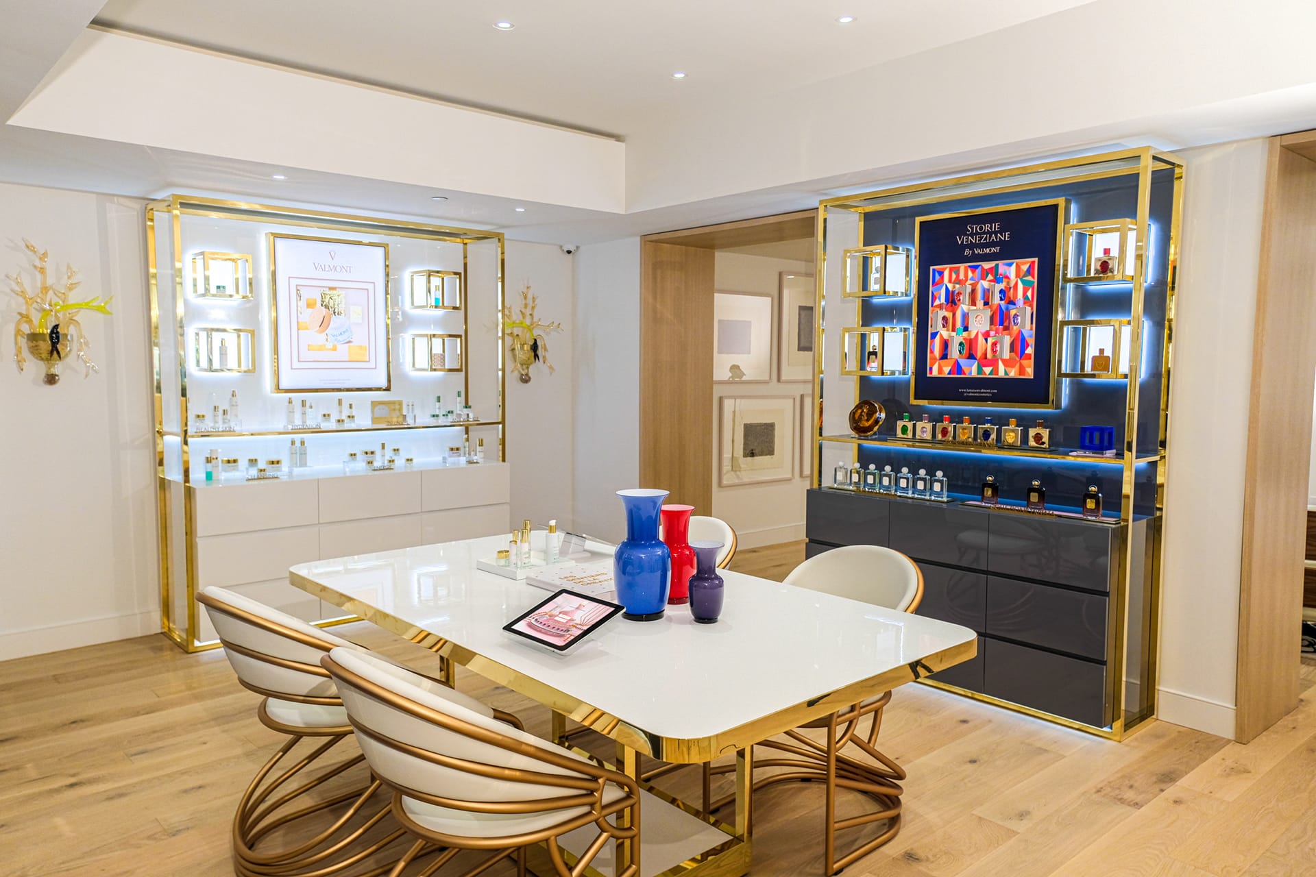 Luxury perfume showroom with gold accents, white table with colorful vases, and shelves displaying various perfume bottles.