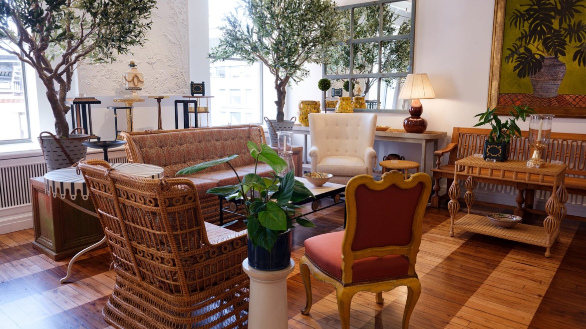 Elegant living room with wicker furniture, large potted plants, decorative wall art, and a wooden floor.