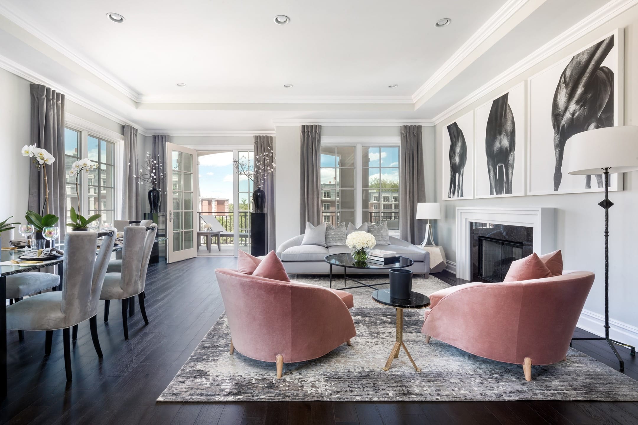Spacious modern living room with pink chairs, large windows, elegant dining area, and black-and-white artwork on the walls.