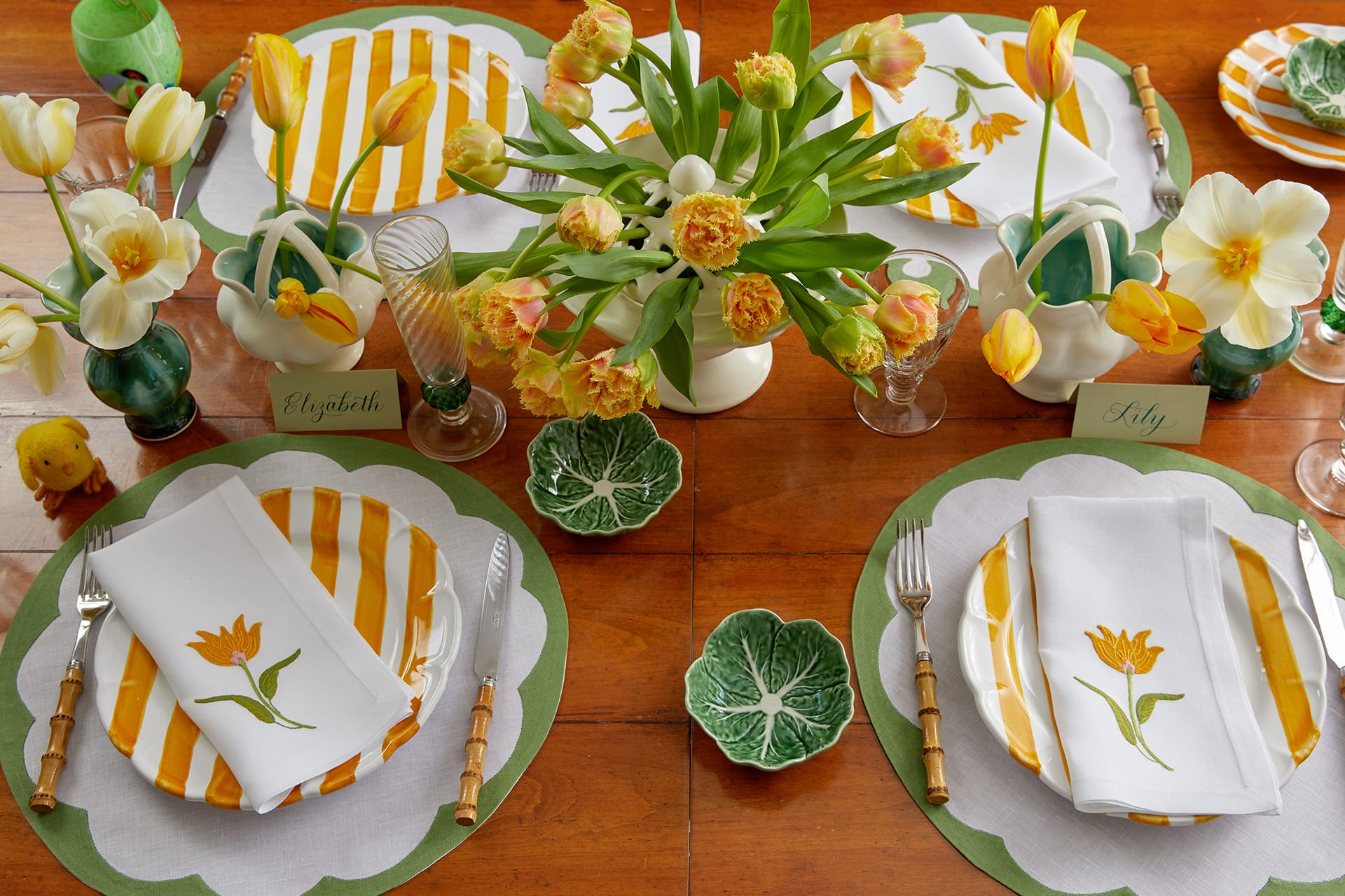 Elegant spring-themed table setting with tulips, striped plates, and personalized name cards on a wooden table.