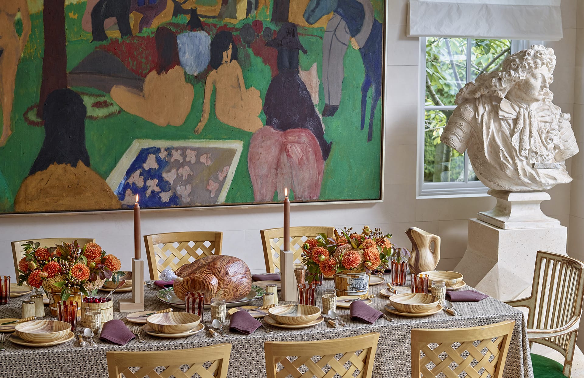 Elegant dining room setup with a decorative table, floral centerpieces, a roast, candles, large painting, and a sculpture.