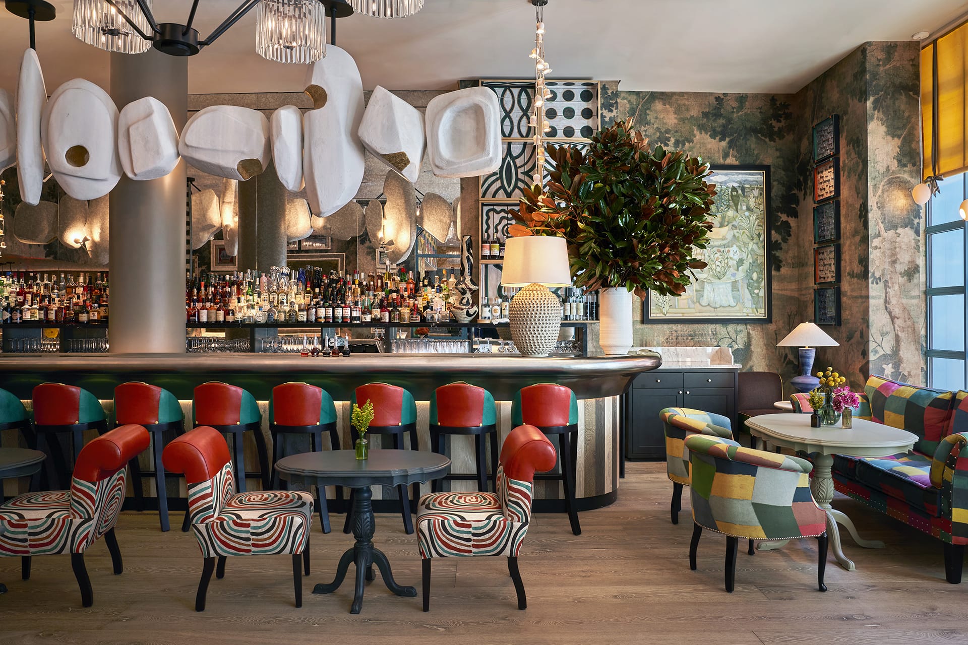 Colorful and eclectic bar interior with vibrant chairs, wooden floor, large plant, and modern decorative elements.