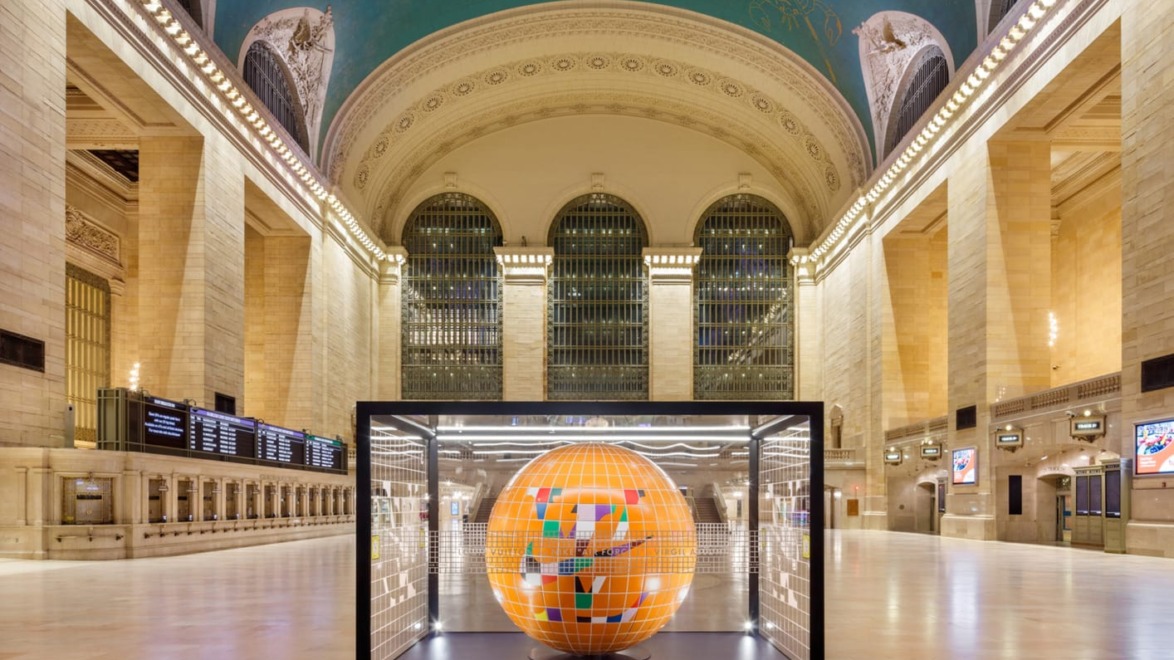 Vibrant art installation of a globe inside a glass case at the spacious and ornate Grand Central Terminal.
