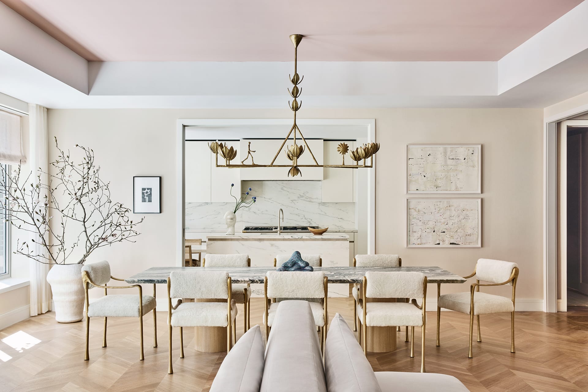 Modern dining room with elegant chandelier, marble table, and cushioned chairs, showcasing minimalist decor with framed art.