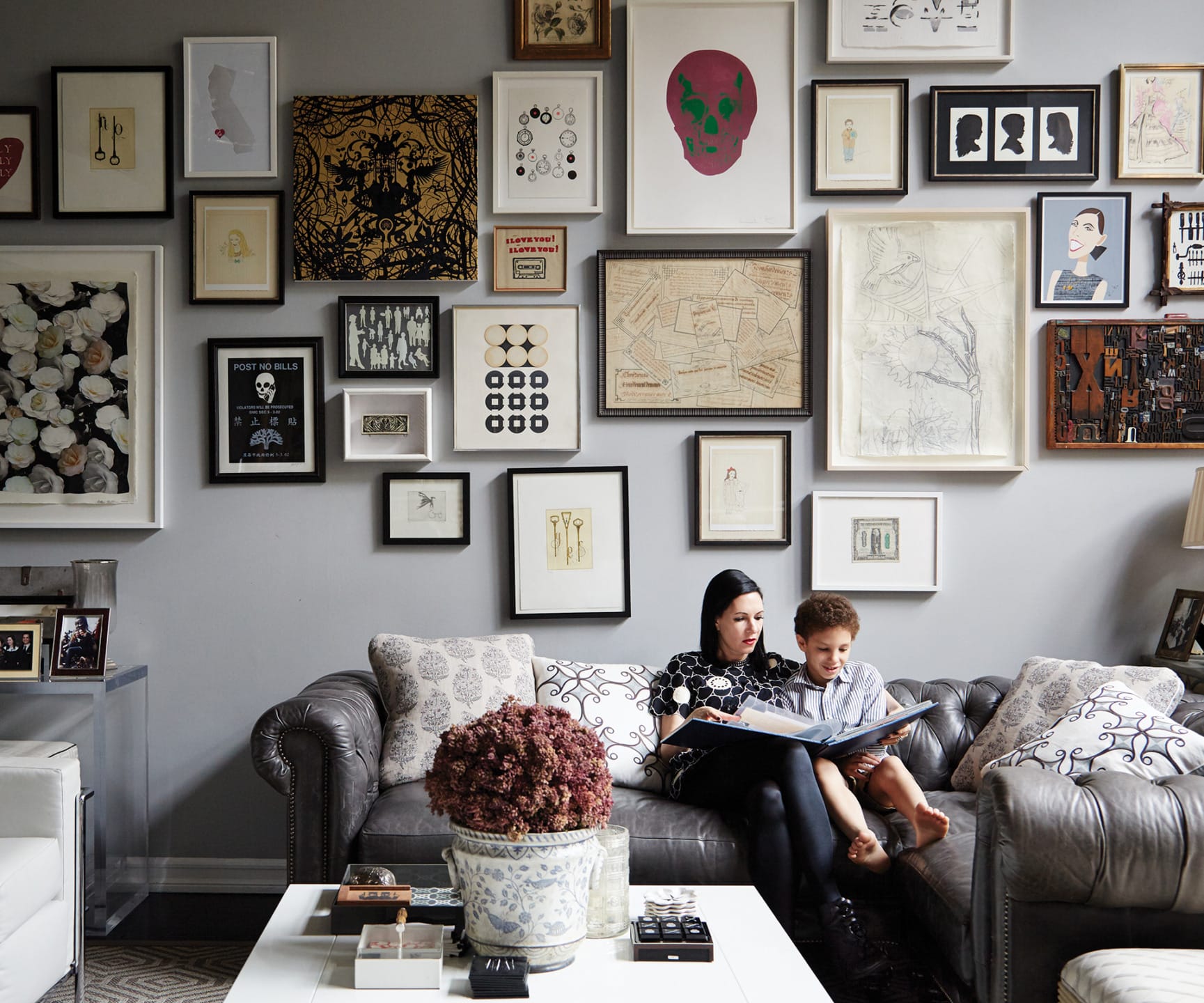 Woman and child sitting on a sofa in a living room with a gallery wall of various art pieces and frames.