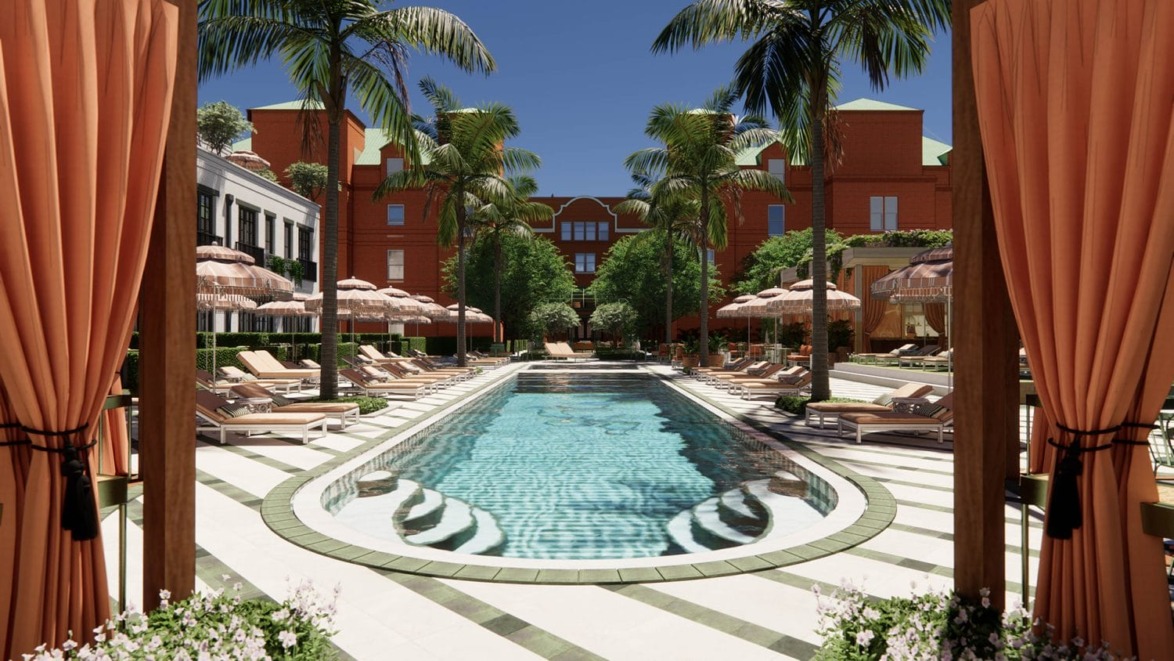 Luxurious outdoor pool surrounded by sun loungers and palm trees with elegant red-brick building in the background