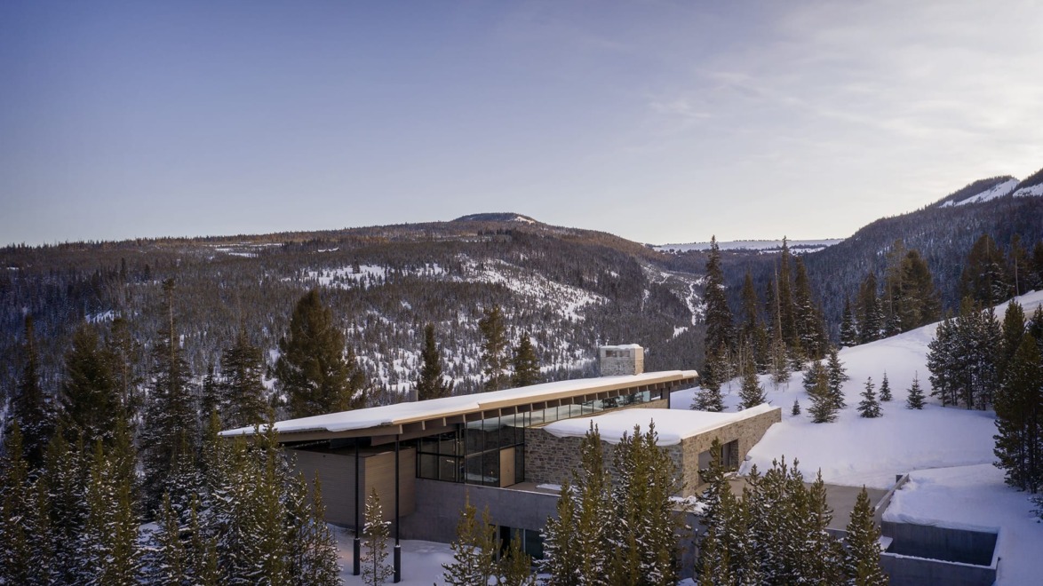 Modern building in snowy mountain landscape surrounded by pine trees under a clear blue sky.