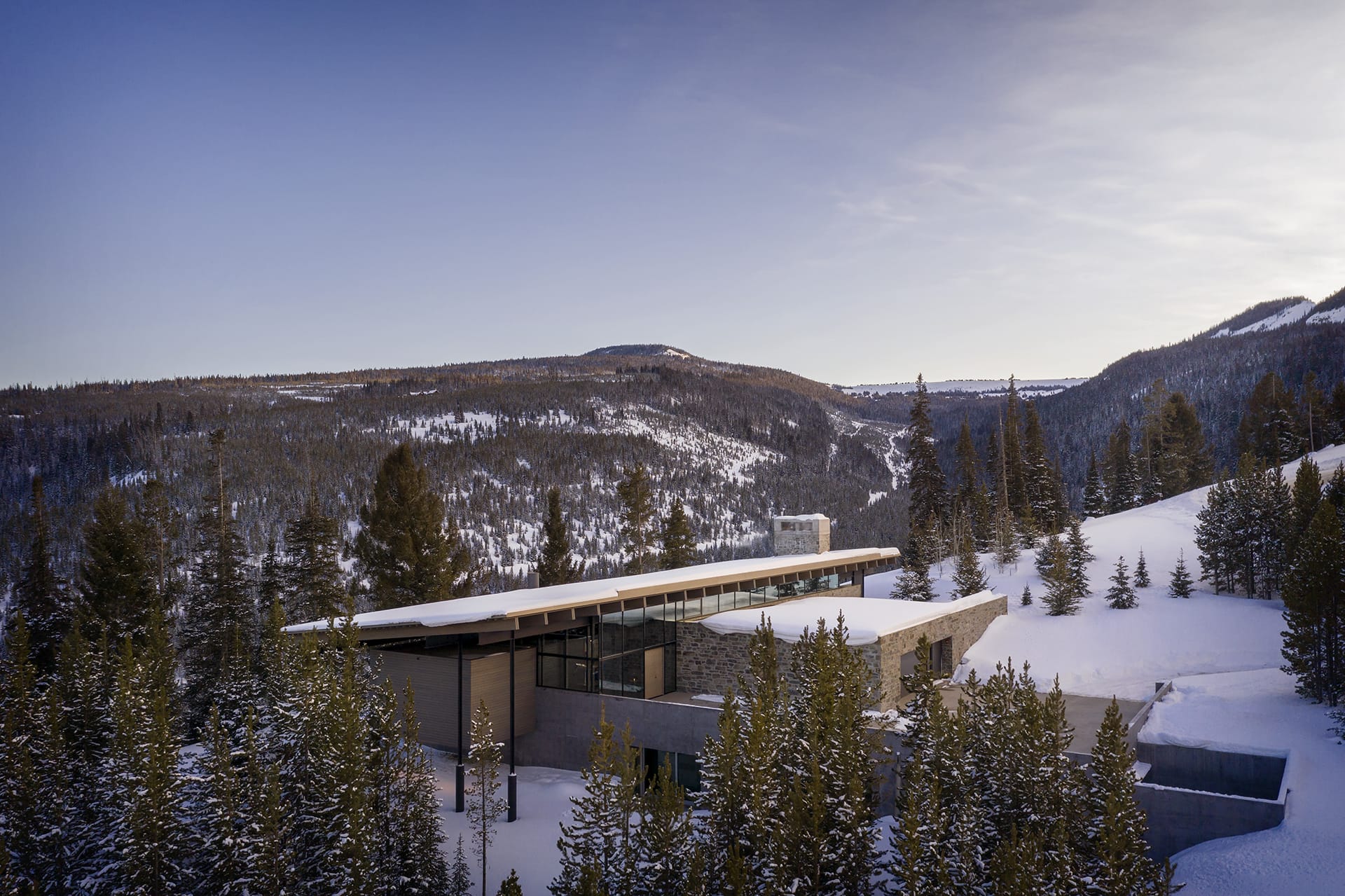 Modern building in snowy mountain landscape surrounded by pine trees under a clear blue sky.